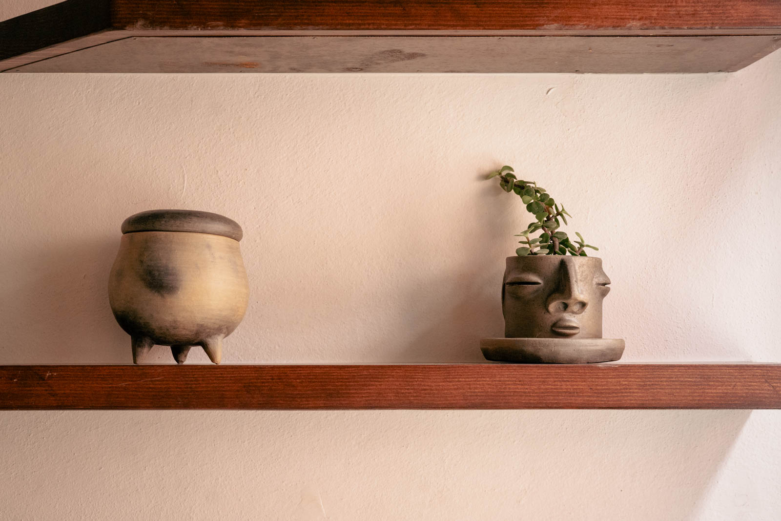 Handmade ceramic pottery and a face planter with a trailing succulent on a wooden shelf inside Casa de Portales